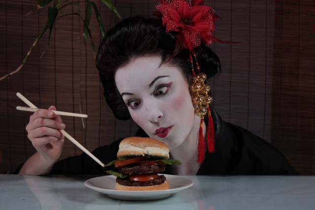 woman eating hamburger with chopsticks